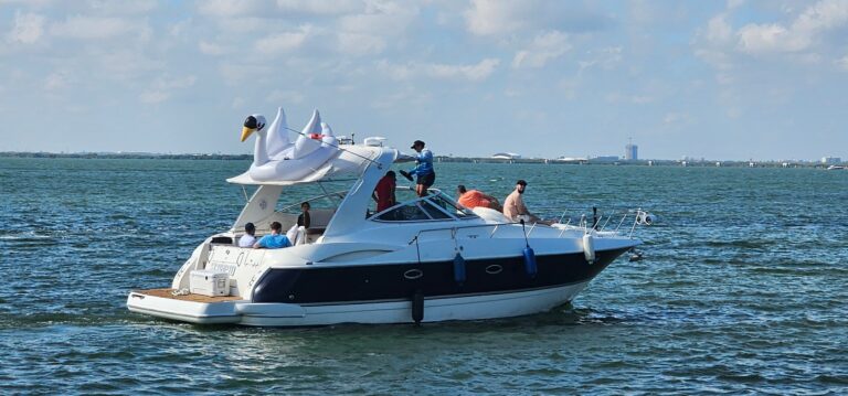 Side view of the white and navy Scorpio Sepress cruiser family yacht with inflatable swan float on deck and guests on board cruising in turquoise Cancun Bay waters