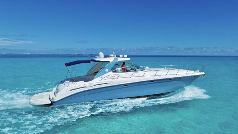 Front quarter side view of 62 ft Sea Ray Sea Whale luxury yacht speeding through turquoise Caribbean water with Cancun skyline in distance