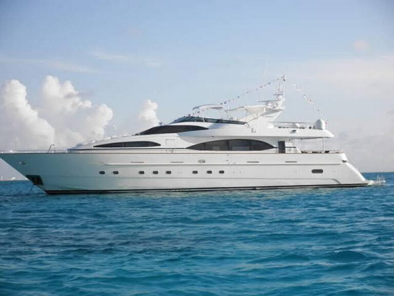 Aerial bow angle of 100 ft Azimut luxury yacht charter anchored in sparkling turquoise Caribbean water off Cancun, side deck and teak swim platform visible with Mexican flag flying
