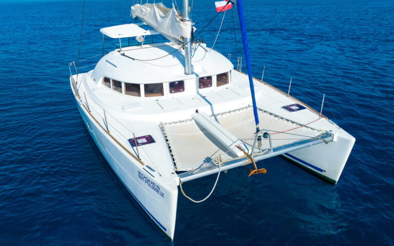 Aerial view of 38 ft Lagoon catamaran sailing under full white mainsail on deep blue Caribbean waters near tropical coastline, Puerto Aventuras sailing charter