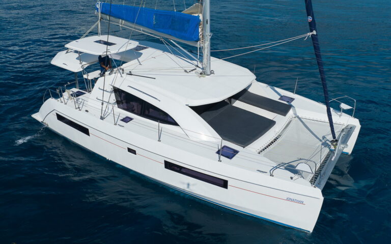 Front bow view of luxury 40 ft Leopard catamaran rental anchored in calm blue Caribbean sea at Puerto Aventuras with Mexican flag flying from the mast