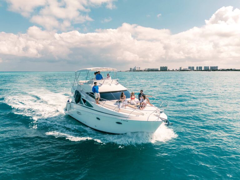 Vista aérea cenital del yate blanco Silverton Manta Ray con flybridge fondeado en aguas turquesas brillantes del Caribe cerca de Cancún con invitados en el asoleadero de proa