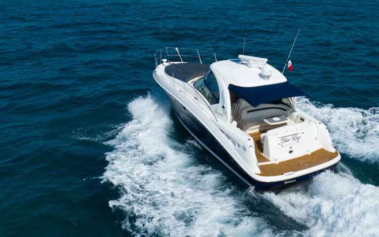 Aerial stern view of 40 ft Sea Ray Sundancer luxury yacht charter cruising at speed in deep blue Caribbean waters near Riviera Maya, Mexican flag flying on stern