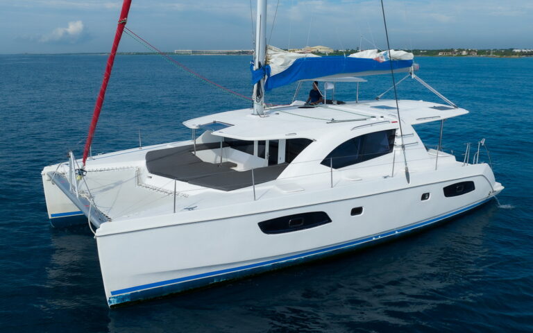 44 ft Leopard catamaran sailing charter under full white mainsail on deep blue Caribbean waters with Riviera Maya coastline in the distance, ideal luxury boat for Cozumel day trips