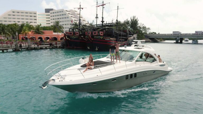 Vista aérea con dron del yate charter de lujo Sea Ray Sundancer Cava 50 ft con invitados en la popa en aguas turquesas del Caribe en Cancún
