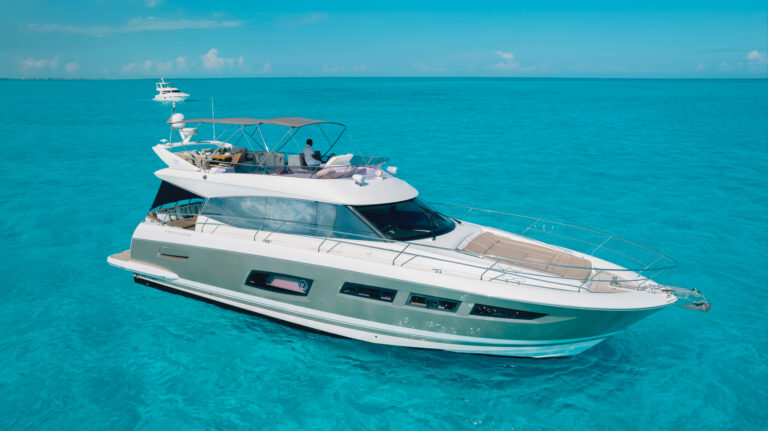 Side aerial view of 60 ft Prestige luxury yacht anchored in crystal-clear turquoise Caribbean water near Cancun with guests on flybridge