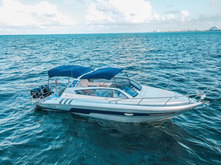 Vista aérea lateral del yate offshore Hanover 305 34 ft con toldo bimini azul y motores fuera de borda gemelos de 300 HP navegando en aguas turquesas resplandecientes del Caribe cerca de Cancún