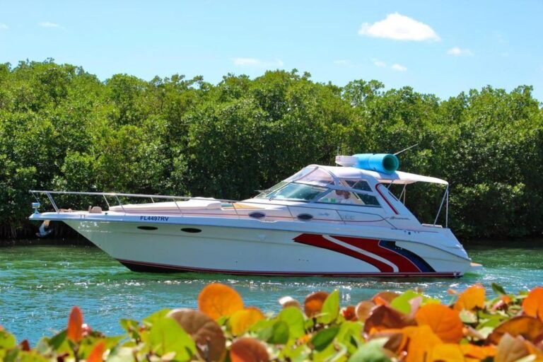 Vista lateral del barco familiar Sea Ray Sundancer Lazy Dayz 35 ft en la laguna de Cancún con franjas gráficas distintivas rojas y azules en el casco y colchoneta azul enrollada en el techo de la cabina