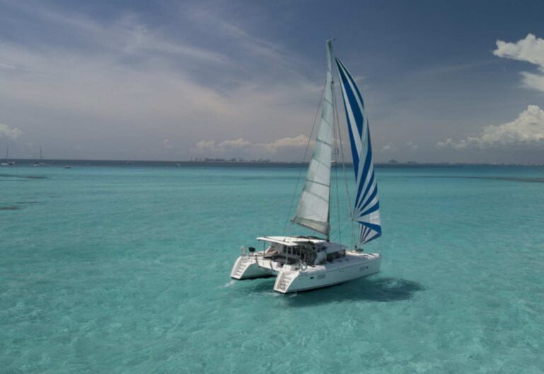Catamarán Lagoon 421 a toda vela con velas azul y blanco navegando en aguas turquesas del Caribe durante un charter VIP todo incluido de Cancún a Isla Mujeres