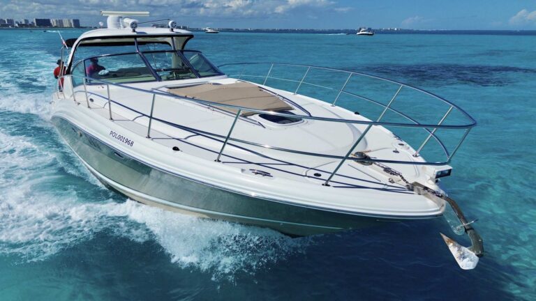 Aerial starboard bow view of 44 ft Sea Ray Sundancer Dolphin Believe luxury yacht charter at speed, white hull with tan bow sun pad, Cancun Hotel Zone coastline in background