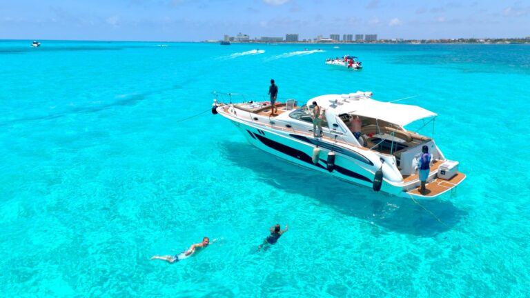 Vista aérea del barco familiar Sea Ray Intrepido 45 ft fondeado en aguas turquesas cristalinas del Caribe cerca de Cancún, con invitados haciendo snorkel al costado y tripulación de pie en cubierta