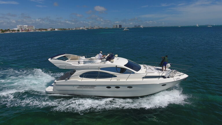 50 ft Azimut Amadeus luxury yacht charter cruising near Isla Mujeres with guests enjoying the open deck, traditional palapa restaurants visible along the rocky coastline
