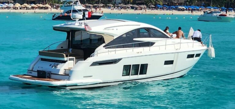 Vista de estribor del yate charter de lujo Fairline GT 50 ft fondeado en aguas turquesas del Caribe con playa bordeada de palmeras al fondo cerca de Cancún