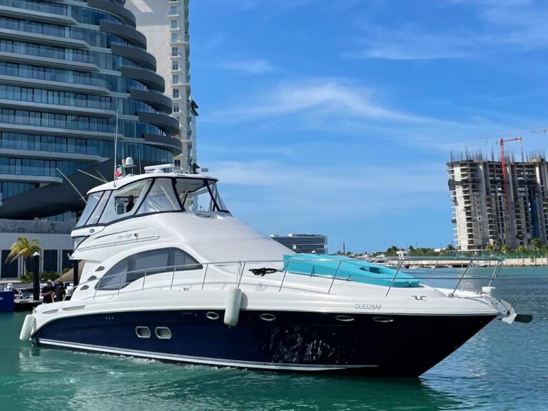 Starboard profile of 58 ft Sea Ray flybridge luxury yacht Neptuno departing Cancun marina, blue hull, turquoise water, modern high-rise towers in background