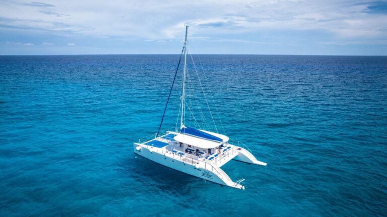 Aerial drone view of large 74 ft catamaran charter for groups up to 50 people sailing on turquoise Caribbean sea at Riviera Maya with blue canopy shade