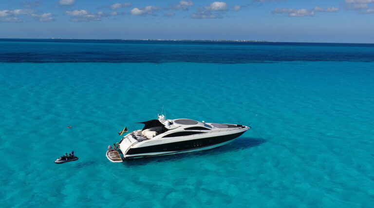 Stern view of 80 ft Sunseeker Predator luxury yacht charter at anchor near sandy beach with teak swim platform and inflatable tender