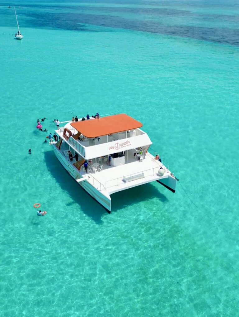 Aerial view of 60 ft MiniDancer catamaran anchored on turquoise Caribbean reef near Isla Mujeres with snorkelers around for group charter rental.