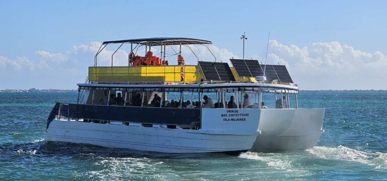 70 ft Obi Kue double-deck catamaran from Isla Mujeres cruising turquoise Caribbean waters with solar panels on the top deck for large group charters.