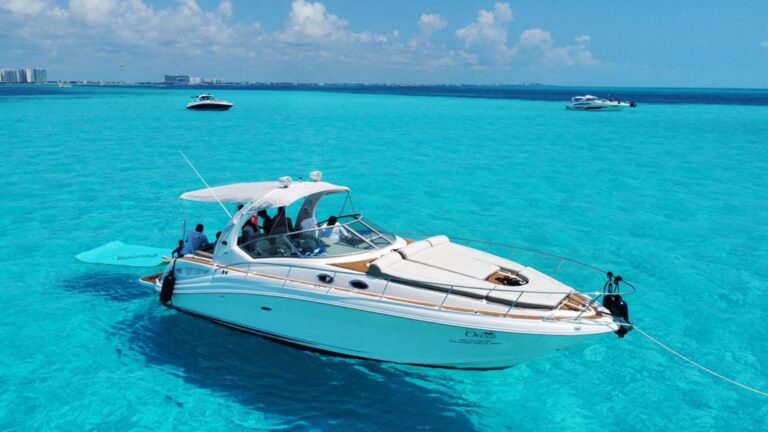 Aerial side view of 37 ft Sea Ray Oasis 340 anchored in turquoise Caribbean water with floating mat deployed, Cancun hotel zone skyline in background.