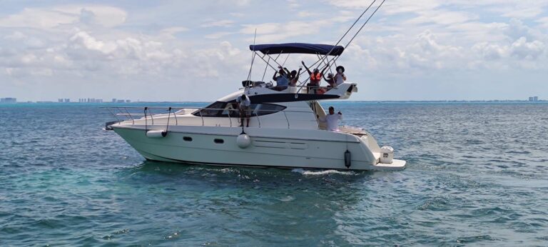 Guests celebrating on flybridge of 40 ft Azimut Good Day luxury yacht anchored in turquoise Caribbean water, Cancun skyline in the distance.