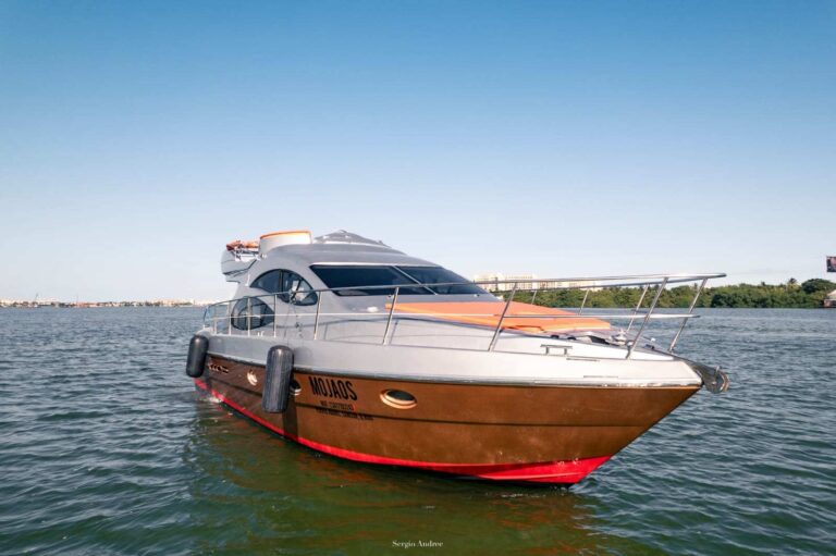 Side profile of 45 ft Azimut Mojaos luxury yacht charter with distinctive golden teak hull and silver superstructure anchored in Cancun lagoon at sunrise.