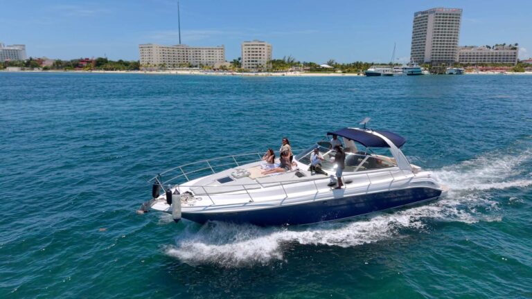 Aerial side view of 45 ft Sea Ray Lorenzo luxury yacht cruising turquoise Caribbean near Cancun hotel zone, guests relaxing on bow sun pad, blue bimini top.