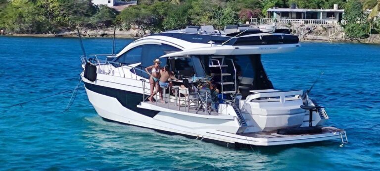 51 ft Galeon 510 Sky luxury yacht charter anchored in turquoise Caribbean water near island with lush greenery, guests enjoying stern cockpit dining, Cancun.