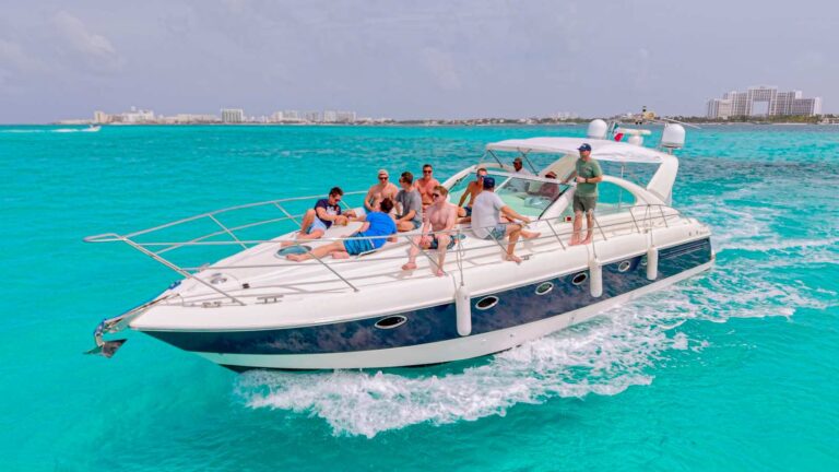 52 ft Fairline luxury yacht charter Nash cruising turquoise Cancun Caribbean with group of 20 guests relaxing on open foredeck and cockpit, hotel zone skyline behind.