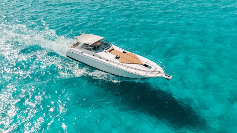 Aerial side view of 55 ft Sea Ray Que Paso Ayer luxury yacht underway in brilliant turquoise Caribbean near Cancun, white hull, teak bow sun pad, bimini canopy.