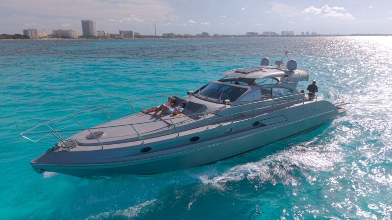 60 ft Ferretti 600 Sport Titanium luxury yacht charter cruising turquoise Caribbean waters off Cancun, guests sunbathing on foredeck, hotel zone skyline behind.