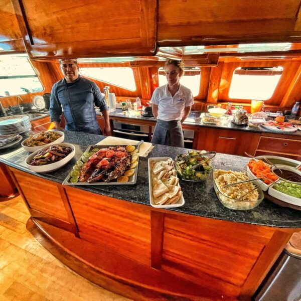 Private chef and crew member behind a yacht galley counter loaded with grilled ribs, fajitas, wraps and fresh salads on board.