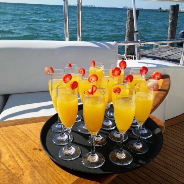 Tray of fresh mimosas garnished with strawberries served on a teak yacht deck overlooking Cancun marina water.