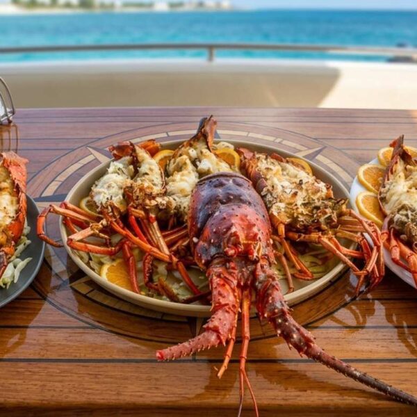 Three plates of grilled lobster tails with citrus served on a teak yacht table by the turquoise Caribbean.