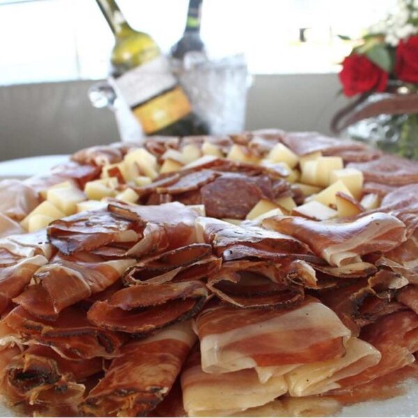 Generous circular charcuterie platter of cured ham, salami and cheese served with chilled wine on board.