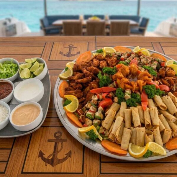 Large catering platter of fried shrimp, taquitos and chicken skewers with dipping sauces on an anchored yacht.