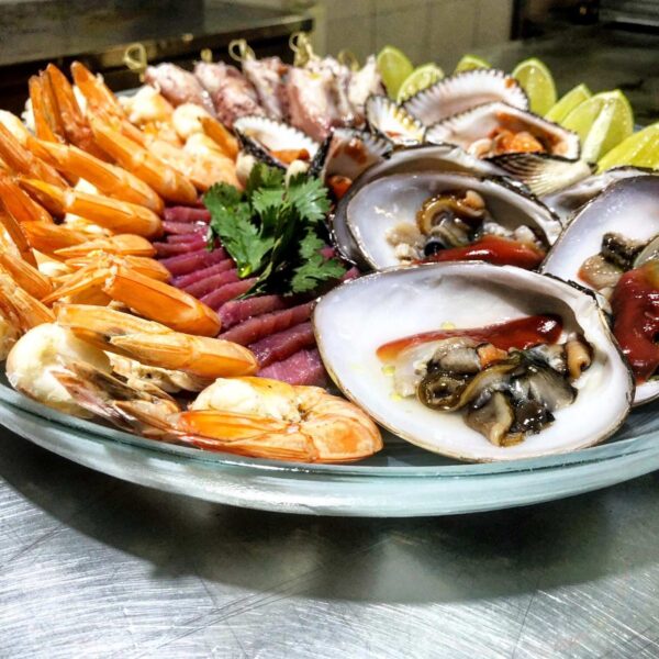 Fresh seafood platter of shrimp, raw oysters, tuna and lime arranged on a glass plate in the galley.
