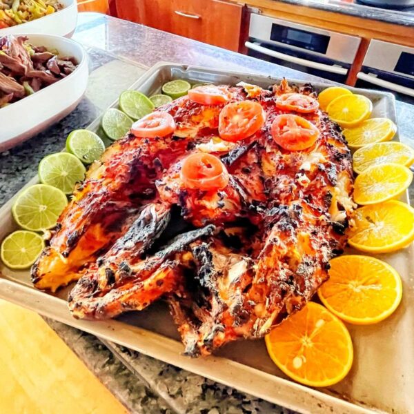 Whole grilled fish garnished with tomato, lime and orange slices beside fajitas on a yacht galley counter.