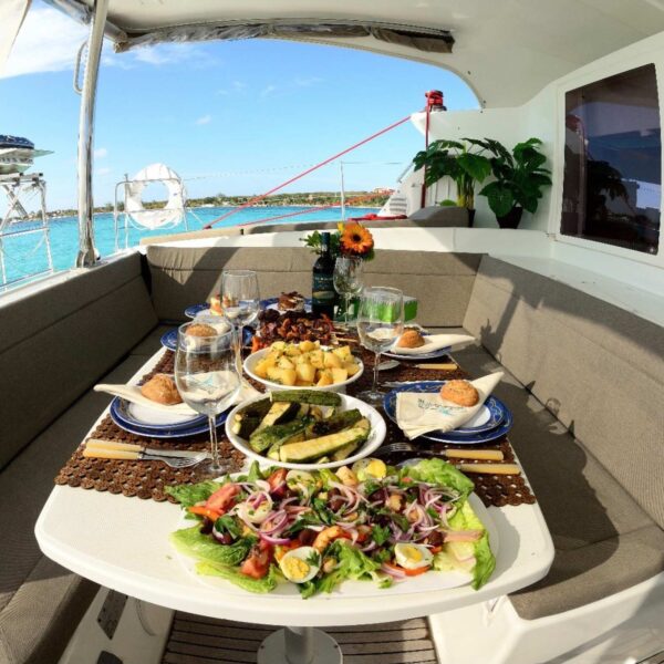 Catamaran cockpit table set with garden salad, grilled zucchini, roasted potatoes and wine by the Caribbean.