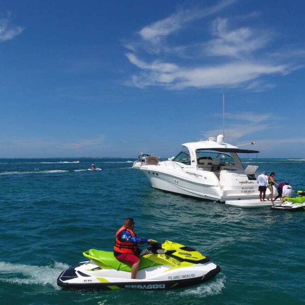 Sea-Doo jet ski rider speeds past a moored yacht and second wave runner during a private Cancun charter on board adventure.