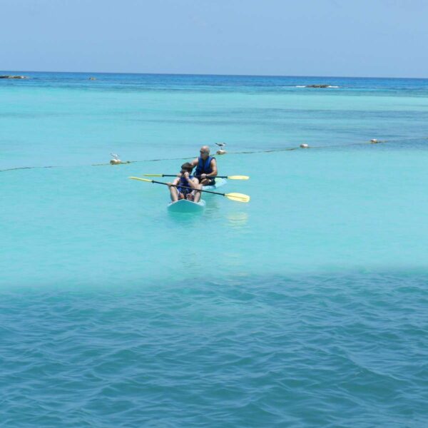 Couple paddles a clear see-through kayak across calm turquoise Caribbean water near Cancun on a relaxed yacht day tour.