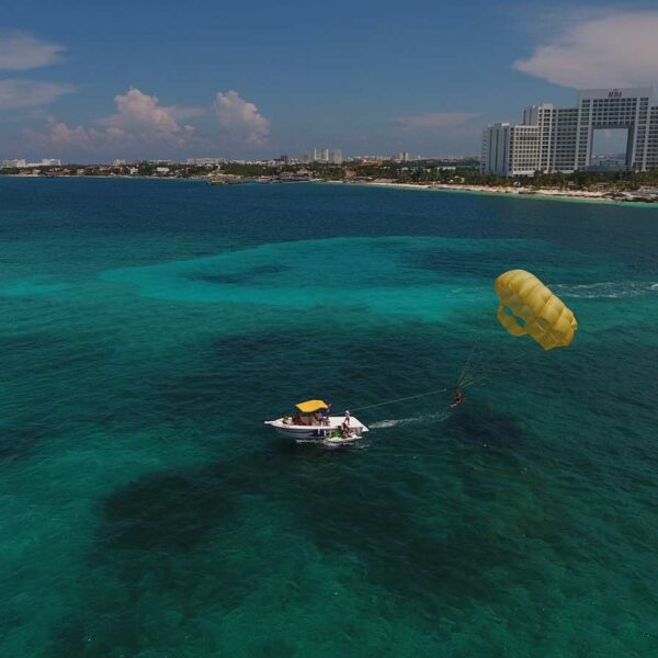 Aerial view of a parasailing boat towing a yellow parachute over reef waters off the Cancun hotel zone beaches.